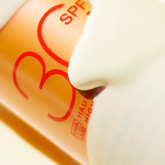 Nuxe Sun Spray SPF30 184 g solkrem for ansikt i bronsefarget sprayflaske som ligger i bølgende blått vann