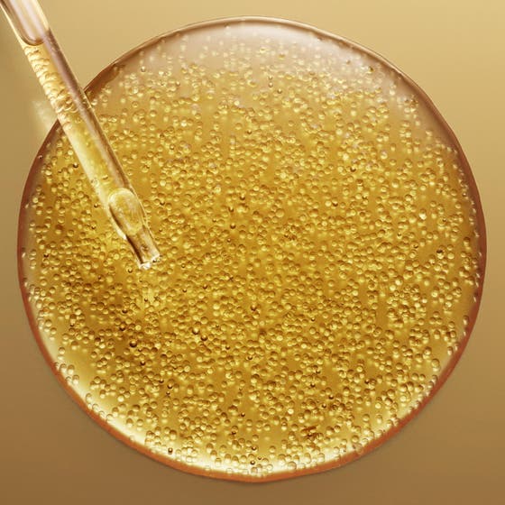 Nuxe Super Serum [10] Eye 15 ml anti-aging øyeserum i gullflaske foran en glitrende bakgrunn av gylne bobler.