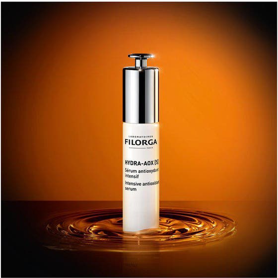 Filorga Hydra-Aox 5 Intensive Antioxidant Serum 30 ml glødgivende ansiktsserum i hvit flaske på en gyllen vannflate