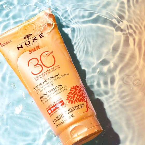 Nuxe Sun Delicious Lotion 150 ml solbeskyttelse SPF30 i oransje tube omgitt av klart, bølgende vann.