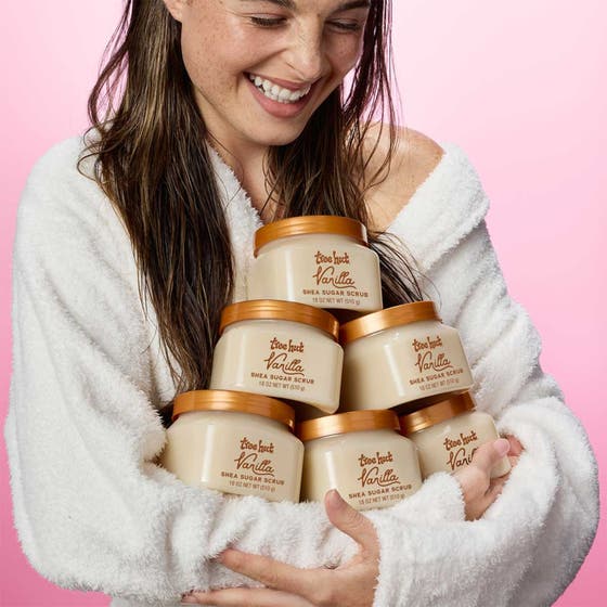 Tree Hut Shea Sugar Scrub Vanilla 510 g exfolierande body scrub hålls av en leende kvinna i vit morgonrock
