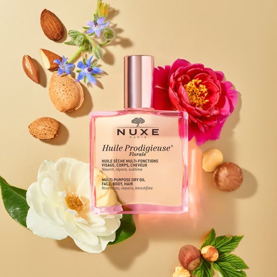 Nuxe Huile Prodigieuse Florale 100 ml pleiende tørrolje i glassflaske med parfyme og dusjgelé på rosa bakgrunn.