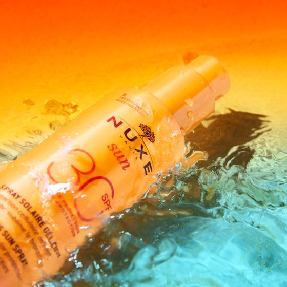 Nuxe Sun Spray SPF30 184 g solbeskyttelse i en oransje sprayflaske som ligger i glitrende blått vann