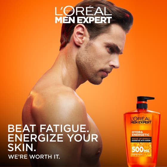 L'Oréal Paris Men Expert Hydra Energetic Shower Gel 1000 ml oppkvikkende dusjsåpe i oransje pumpeflaske ved siden av en mann