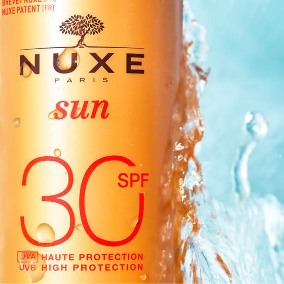 Nuxe Sun Spray SPF30 184 g solkrem med hvit kremet tekstur som renner over den oransje flasken