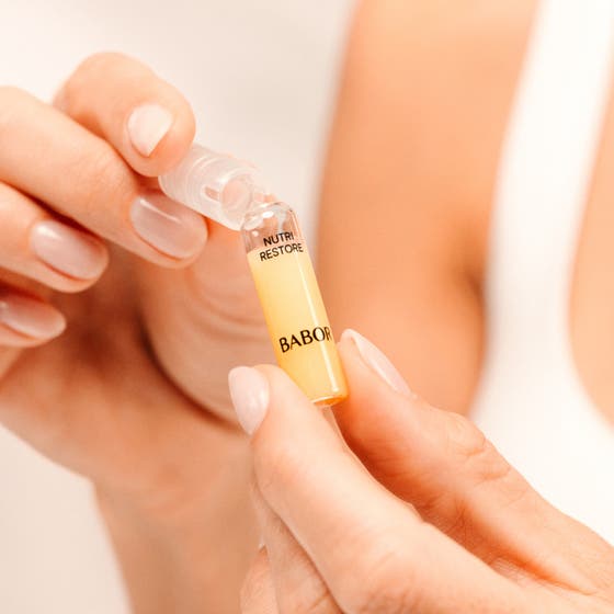 Babor Nutri Restore Ampoule 14 ml serum som dryppes fra en glassampulle i håndflaten for pleie.