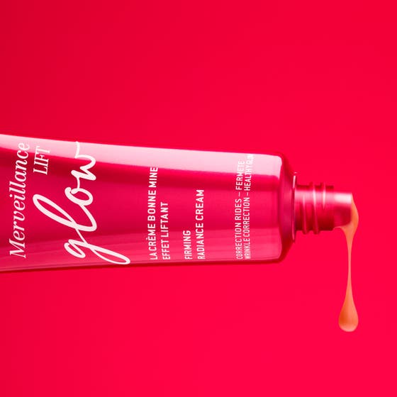 Nuxe Merveillance Lift Glow 50 ml kiinteyttävä päivävoide ja sen heleyttävä persikkainen koostumus pinkillä taustalla.
